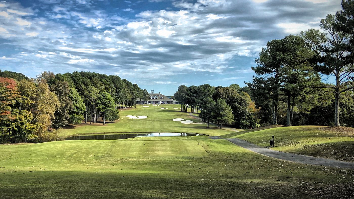 The 18th fairway at Legends, lined with pines, running past a pond toward the clubhouse.