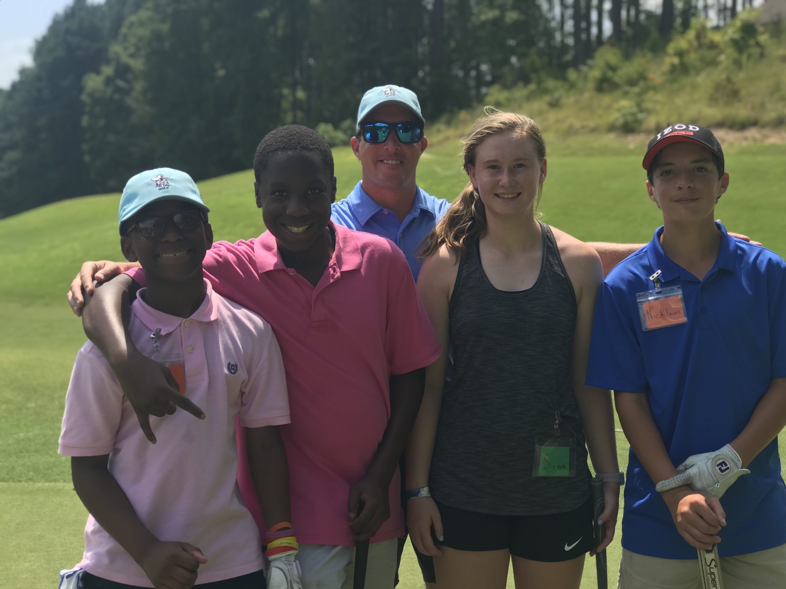 A group of juniors and a coach smile together on a golf course.